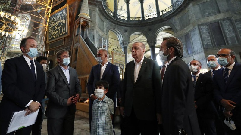 Turkey's President Recep Tayyip Erdogan, center, salutes supporters as he visits the Byzantine-era Hagia Sophia, in the background, one of Istanbul's main tourist attractions in the historic Sultanahmet district of Istanbul, Sunday, July 19, 2020, days after he formally reconverted Hagia Sophia into a mosque and declared it open for Muslim worship, after a high court annulled a 1934 decision that had made the religious landmark a museum.(Turkish Presidency via AP, Pool)