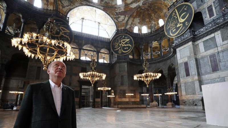 Turkey's President Recep Tayyip Erdogan, center, salutes supporters as he visits the Byzantine-era Hagia Sophia, in the background, one of Istanbul's main tourist attractions in the historic Sultanahmet district of Istanbul, Sunday, July 19, 2020, days after he formally reconverted Hagia Sophia into a mosque and declared it open for Muslim worship, after a high court annulled a 1934 decision that had made the religious landmark a museum.(Turkish Presidency via AP, Pool)