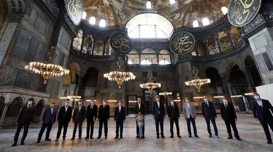 Turkey's President Recep Tayyip Erdogan, center, salutes supporters as he visits the Byzantine-era Hagia Sophia, in the background, one of Istanbul's main tourist attractions in the historic Sultanahmet district of Istanbul, Sunday, July 19, 2020, days after he formally reconverted Hagia Sophia into a mosque and declared it open for Muslim worship, after a high court annulled a 1934 decision that had made the religious landmark a museum.(Turkish Presidency via AP, Pool)