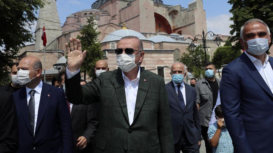 Turkey's President Recep Tayyip Erdogan, center, salutes supporters as he visits the Byzantine-era Hagia Sophia, in the background, one of Istanbul's main tourist attractions in the historic Sultanahmet district of Istanbul, Sunday, July 19, 2020, days after he formally reconverted Hagia Sophia into a mosque and declared it open for Muslim worship, after a high court annulled a 1934 decision that had made the religious landmark a museum.(Turkish Presidency via AP, Pool)