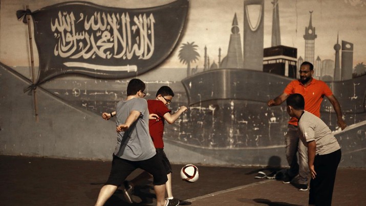 People play soccer in a public park past a wall art showing Saudi's flag and landmarks, in Jiddah, Saudi Arabia, Monday, Oct. 21, 2019. (AP Photo/Amr Nabil)