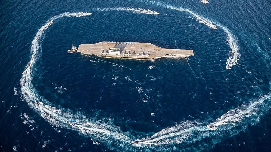 In this photo released Tuesday, July 28, 2020, by Sepahnews, Revolutionary Guard's speed boats circle around a replica aircraft carrier during a military exercise. Iran’s paramilitary Revolutionary Guard has fired a missile from a helicopter targeting the mock-up aircraft carrier in the strategic Strait of Hormuz. That's according to footage aired on state television on Tuesday. Iranian commandos also fast-roped down from a helicopter onto the replica in the footage from the exercise called “Great Prophet 14.” The drill appears aimed at threatening the U.S. amid tensions between Tehran and Washington. (Sepahnews via AP)