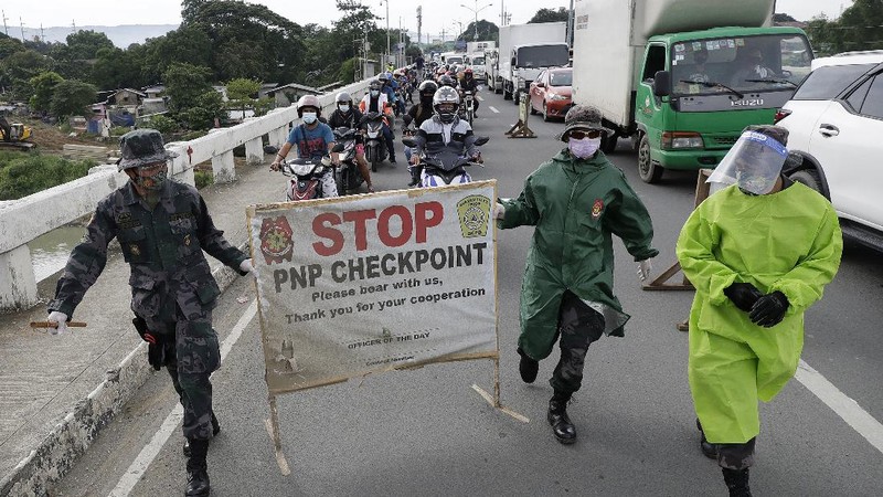 Police officers wearing protective gear carry a checkpoint sign on a roadway Tuesday, Aug. 4, 2020, outside Manila, Philippines, as the capital is placed on another lockdown in the hopes of controlling the surge of coronavirus cases. Commuter trains, buses and other public vehicles stayed off the main roads of the Philippine capital Tuesday and police were again staffing checkpoints to restrict public travel. (AP Photo/Aaron Favila)