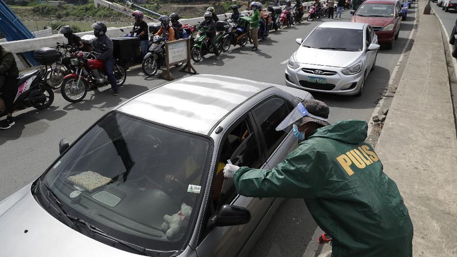 Police officers wearing protective gear carry a checkpoint sign on a roadway Tuesday, Aug. 4, 2020, outside Manila, Philippines, as the capital is placed on another lockdown in the hopes of controlling the surge of coronavirus cases. Commuter trains, buses and other public vehicles stayed off the main roads of the Philippine capital Tuesday and police were again staffing checkpoints to restrict public travel. (AP Photo/Aaron Favila)