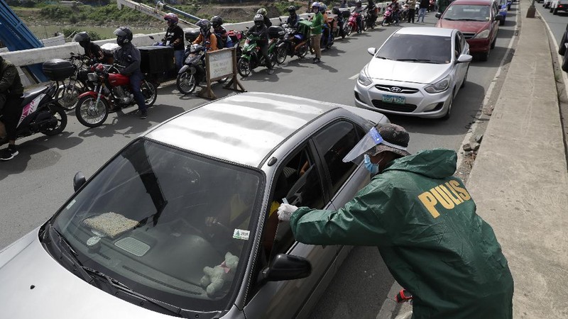 Police officers wearing protective gear carry a checkpoint sign on a roadway Tuesday, Aug. 4, 2020, outside Manila, Philippines, as the capital is placed on another lockdown in the hopes of controlling the surge of coronavirus cases. Commuter trains, buses and other public vehicles stayed off the main roads of the Philippine capital Tuesday and police were again staffing checkpoints to restrict public travel. (AP Photo/Aaron Favila)