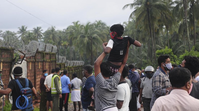 Officials stand by the debris of the Air India Express flight that skidded off a runway while landing in Kozhikode, Kerala state, India, Saturday, Aug. 8, 2020. The special evacuation flight bringing people home to India who had been trapped abroad because of the coronavirus skidded off the runway and split in two while landing in heavy rain killing more than a dozen people and injuring dozens more. (AP Photo/Shijith Sreedhar)