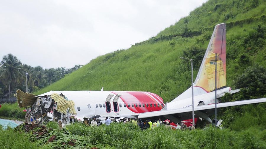 Officials stand by the debris of the Air India Express flight that skidded off a runway while landing in Kozhikode, Kerala state, India, Saturday, Aug. 8, 2020. The special evacuation flight bringing people home to India who had been trapped abroad because of the coronavirus skidded off the runway and split in two while landing in heavy rain killing more than a dozen people and injuring dozens more. (AP Photo/Shijith Sreedhar)