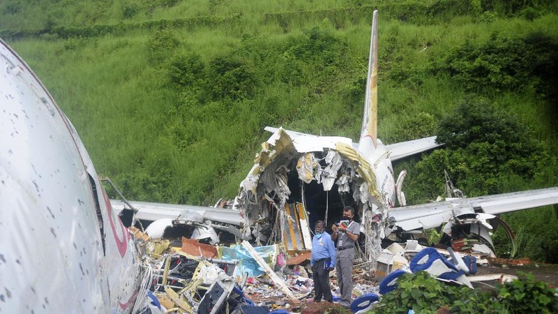 Officials stand by the debris of the Air India Express flight that skidded off a runway while landing in Kozhikode, Kerala state, India, Saturday, Aug. 8, 2020. The special evacuation flight bringing people home to India who had been trapped abroad because of the coronavirus skidded off the runway and split in two while landing in heavy rain killing more than a dozen people and injuring dozens more. (AP Photo/Shijith Sreedhar)
