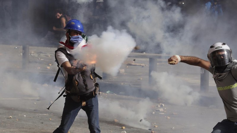 Anti-government protesters clash with riot police officers during a protest against the political elites and the government after this week's deadly explosion at Beirut port which devastated large parts of the capital in Beirut, Lebanon, Saturday, Aug. 8, 2020. (AP Photo/Hassan Ammar)