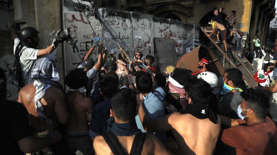 Anti-government protesters clash with riot police officers during a protest against the political elites and the government after this week's deadly explosion at Beirut port which devastated large parts of the capital in Beirut, Lebanon, Saturday, Aug. 8, 2020. (AP Photo/Hassan Ammar)