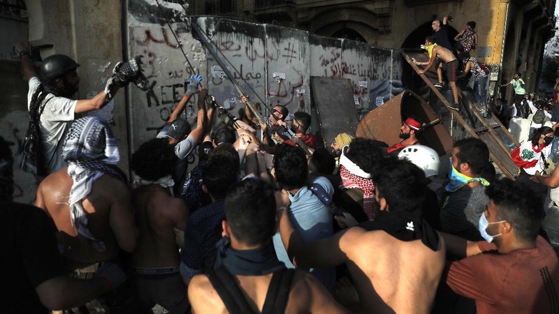 Anti-government protesters clash with riot police officers during a protest against the political elites and the government after this week's deadly explosion at Beirut port which devastated large parts of the capital in Beirut, Lebanon, Saturday, Aug. 8, 2020. (AP Photo/Hassan Ammar)