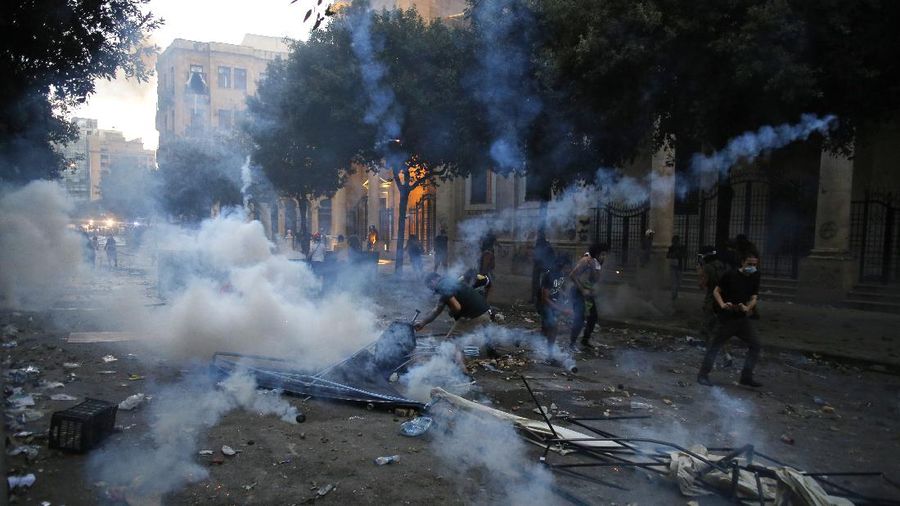 Anti-government protesters clash with riot police officers during a protest against the political elites and the government after this week's deadly explosion at Beirut port which devastated large parts of the capital in Beirut, Lebanon, Saturday, Aug. 8, 2020. (AP Photo/Hassan Ammar)