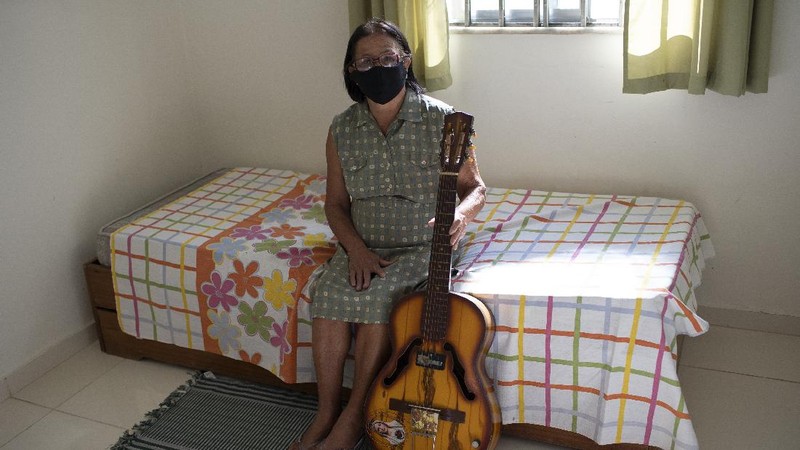 A man dressed in a Batman costume holds a sign with a message that reads in Portuguese: 