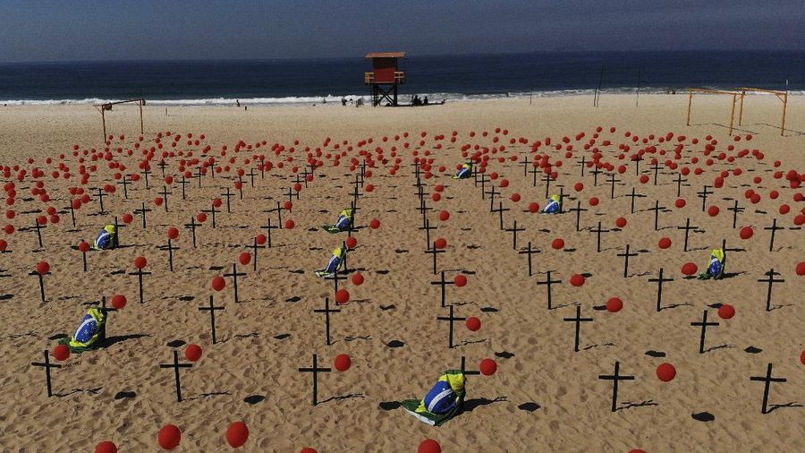 Crosses and red balloons are placed in the sand on Copacabana beach in a demonstration organized by Rio de Paz to honor the victims of COVID-19, as the country heads to a milestone of 100,000 new coronavirus related deaths, in Rio de Janeiro, Brazil, Saturday, Aug. 8, 2020. (AP Photo/Mario Lobao)