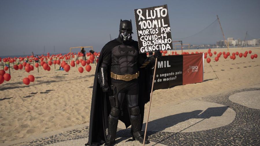 A man dressed in a Batman costume holds a sign with a message that reads in Portuguese: 