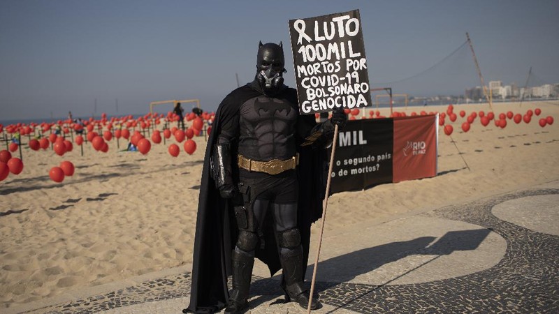 A man dressed in a Batman costume holds a sign with a message that reads in Portuguese: 