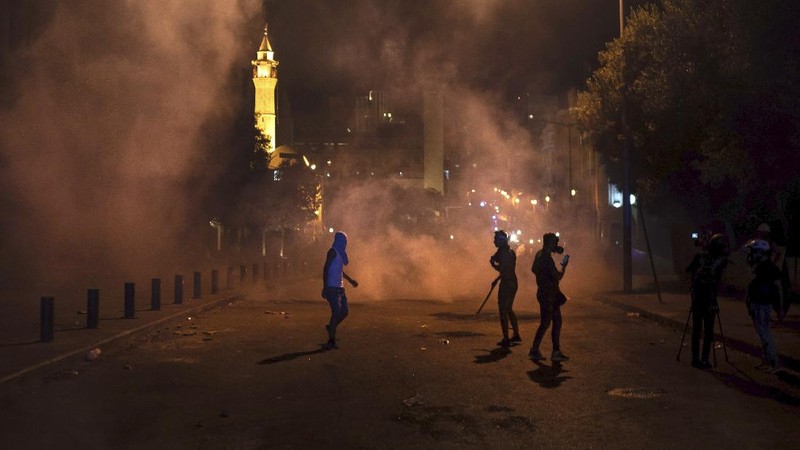 A protester throw stones against the Lebanese riot police, during anti-government protest following Tuesday's massive explosion which devastated Beirut, Lebanon, Sunday, Aug. 9. 2020. (AP Photo/Hussein Malla)