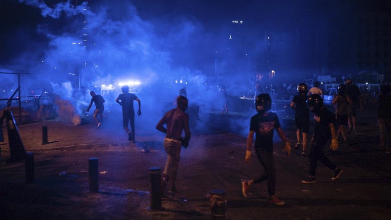 A protester throw stones against the Lebanese riot police, during anti-government protest following Tuesday's massive explosion which devastated Beirut, Lebanon, Sunday, Aug. 9. 2020. (AP Photo/Hussein Malla)