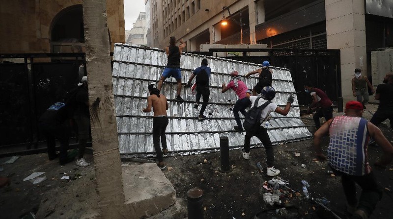 A protester throw stones against the Lebanese riot police, during anti-government protest following Tuesday's massive explosion which devastated Beirut, Lebanon, Sunday, Aug. 9. 2020. (AP Photo/Hussein Malla)