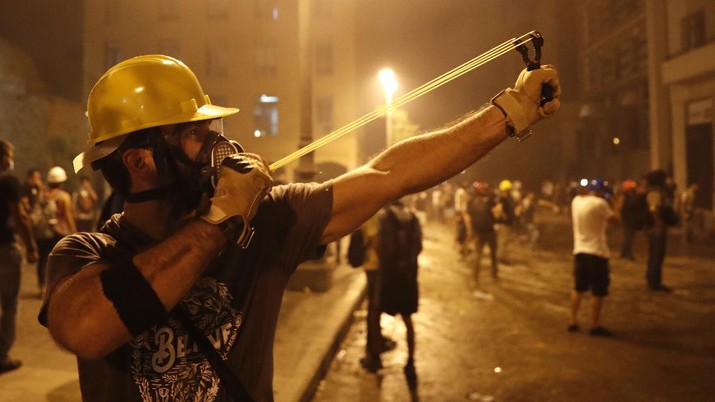 A protester uses a slingshot toward the Lebanese riot police, during anti-government protest following Tuesday's massive explosion which devastated Beirut, Lebanon, Sunday, Aug. 9. 2020. (AP Photo/Hussein Malla)