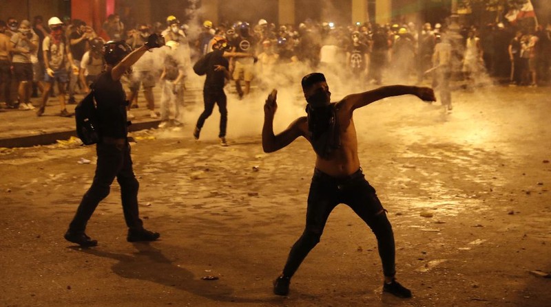 A protester throw stones against the Lebanese riot police, during anti-government protest following Tuesday's massive explosion which devastated Beirut, Lebanon, Sunday, Aug. 9. 2020. (AP Photo/Hussein Malla)