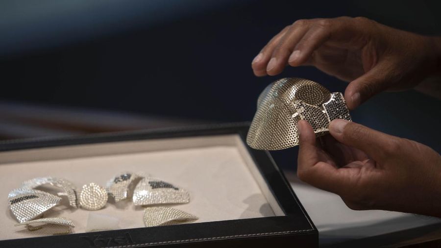 Isaac Levy, owner of Israeli jewelry company Yvel looks at a worker and parts of a mask in Motza near Jerusalem, Sunday, Aug. 9, 2020. An Israeli jewelry company is working on what it says will be the world's most expensive coronavirus mask, a gold, diamond-encrusted face covering with a price tag of $1. 5 million. (AP Photo/Sebastian Scheiner)