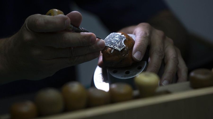 Isaac Levy, owner of Israeli jewelry company Yvel looks at a worker and parts of a mask in Motza near Jerusalem, Sunday, Aug. 9, 2020. An Israeli jewelry company is working on what it says will be the world's most expensive coronavirus mask, a gold, diamond-encrusted face covering with a price tag of $1. 5 million. (AP Photo/Sebastian Scheiner)