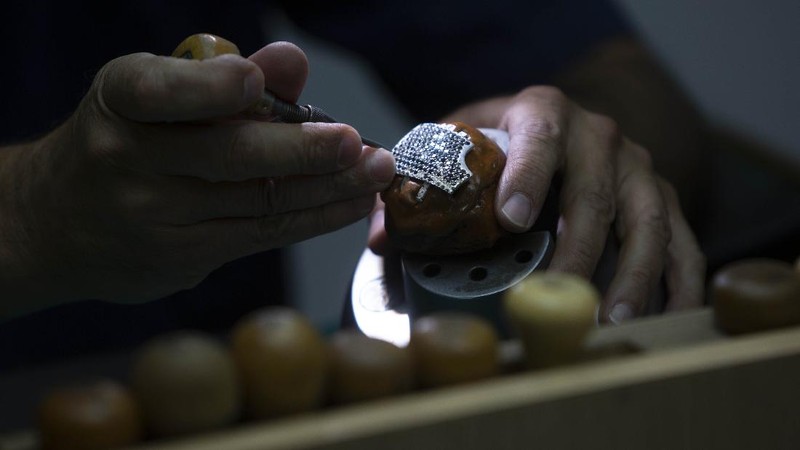 Isaac Levy, owner of Israeli jewelry company Yvel looks at a worker and parts of a mask in Motza near Jerusalem, Sunday, Aug. 9, 2020. An Israeli jewelry company is working on what it says will be the world's most expensive coronavirus mask, a gold, diamond-encrusted face covering with a price tag of $1. 5 million. (AP Photo/Sebastian Scheiner)