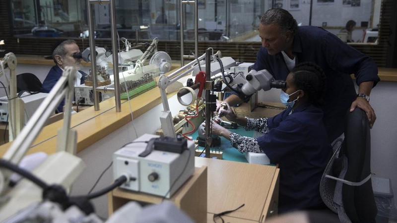 Isaac Levy, owner of Israeli jewelry company Yvel looks at a worker and parts of a mask in Motza near Jerusalem, Sunday, Aug. 9, 2020. An Israeli jewelry company is working on what it says will be the world's most expensive coronavirus mask, a gold, diamond-encrusted face covering with a price tag of $1. 5 million. (AP Photo/Sebastian Scheiner)