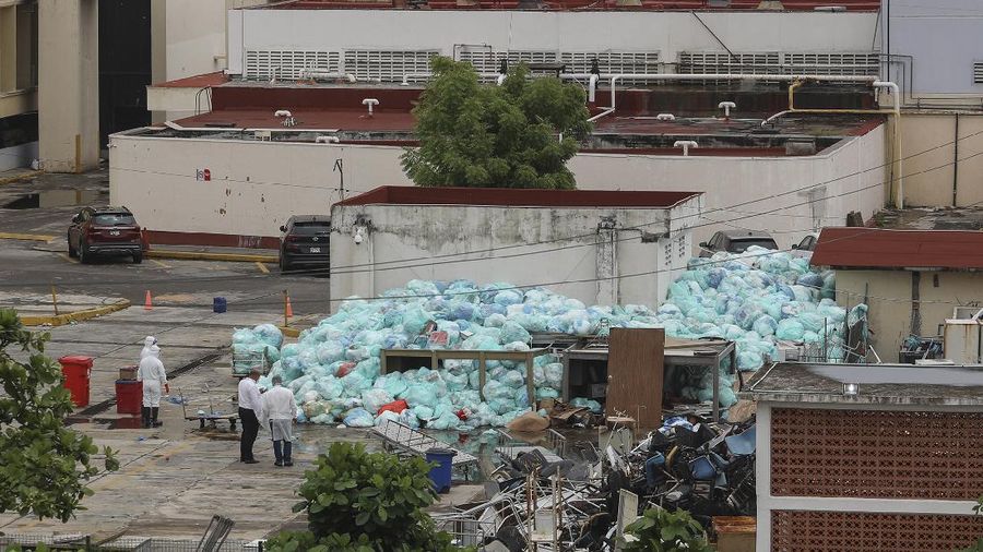 Medical workers using protective equipment dispose of trash bags containing hazardous biological waste into a large pile outside the Hospital del Instituto Mexicano del Seguro Social, which treats patients with COVID-19 in Veracruz, Mexico, Wednesday, Aug. 12, 2020. Improper disposal of medical waste has become an increasing problem in Mexico amid the pandemic. (AP Photo/Felix Marquez)