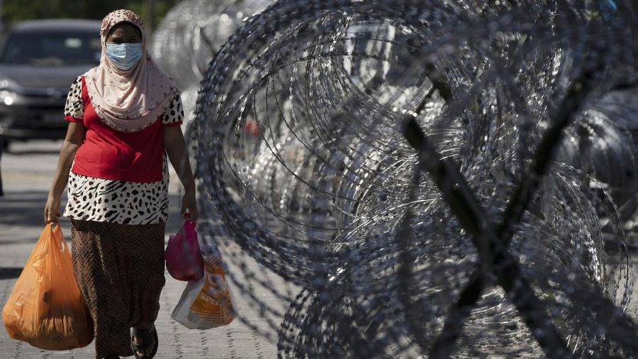 A woman walks home with groceries next to barbed wire in the coronavirus locked down area of Selayang Baru, in Kuala Lumpur, Malaysia, on Sunday, May 3, 2020. The Malaysian Prime Minister Muhyiddin Yassin says the economy needs to be revived as billions have been lost during the partial lockdown that began in March. (AP Photo/Vincent Thian)