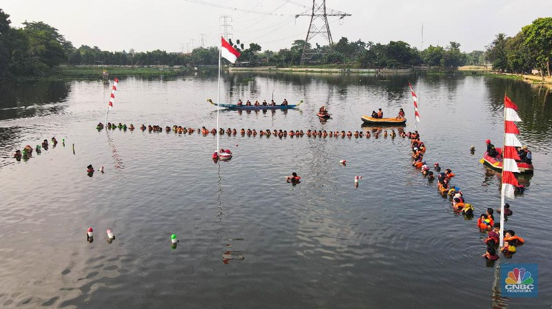 Petugas pengibar bendera melakukan pengibaran bendera Merah Putih pada peringatan HUT Kemerdekaan ke-75 RI di tengah Situ 7 Muara Pamulang, Tangerang Selatan, Banten, Senin (17/8/2020). Upacara yang diikuti oleh ratusan aktivis lingkungan hidup dan juga organisasi kepemudaan iini bertujuan agar pemerintah terus menjaga keberadaan situ yang ada di manapun. (CNBC Indonesia/ Andrean Kristianto)