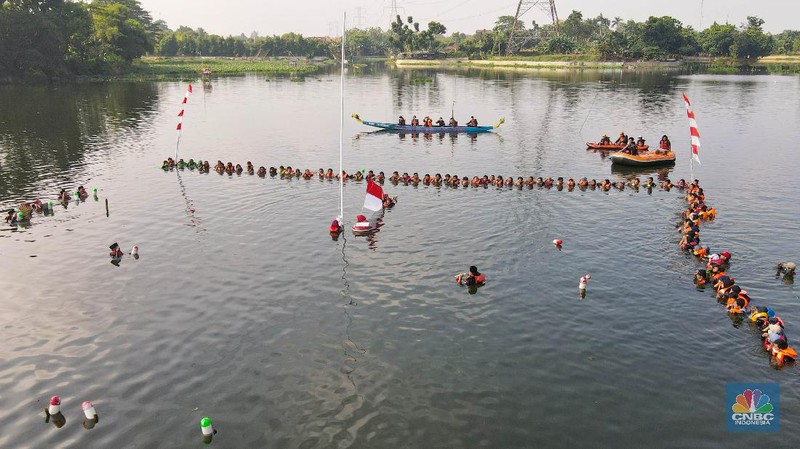 Petugas pengibar bendera melakukan pengibaran bendera Merah Putih pada peringatan HUT Kemerdekaan ke-75 RI di tengah Situ 7 Muara Pamulang, Tangerang Selatan, Banten, Senin (17/8/2020). Upacara yang diikuti oleh ratusan aktivis lingkungan hidup dan juga organisasi kepemudaan iini bertujuan agar pemerintah terus menjaga keberadaan situ yang ada di manapun. (CNBC Indonesia/ Andrean Kristianto)
