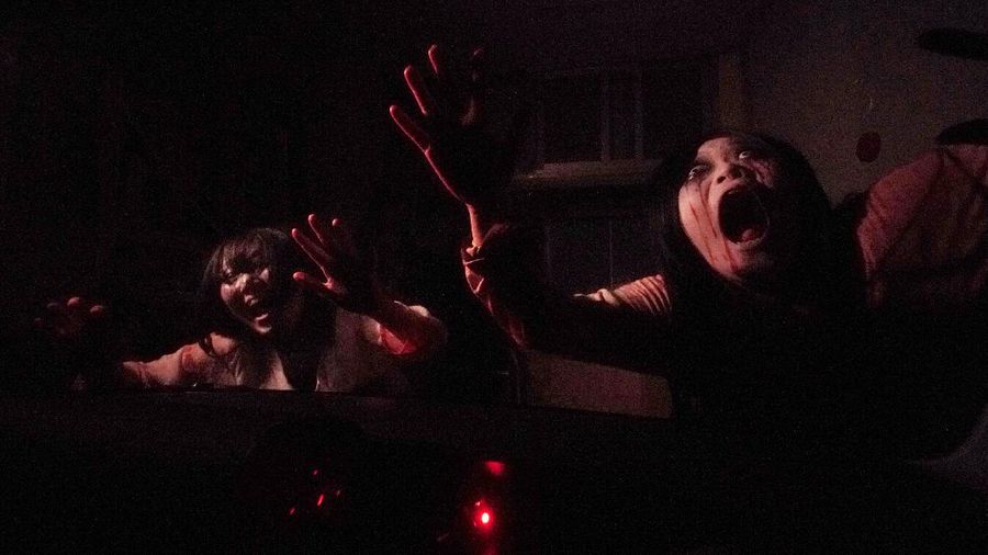 Casts as zombies perform by the window of a vehicle during a demonstration of a drive-in haunted house show at a garage Tuesday, Aug. 18, 2020, in Tokyo. Visitors remain in vehicles as taking prevention measures against the COVID-19 pandemic, while ghosts, zombies and other characters spook the visitors. Visitors could experience the entertainment with the safety of being inside their own vehicles. Or, a vehicle provided by the program is also available for rent at the site. (AP Photo/Eugene Hoshiko)