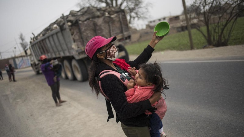 Jenny Diaz begs in the middle of a road while carrying her daughter Aina Flores, 1, on the outskirts of Lima, Peru, Saturday, Aug.22, 2020, amid the coronavirus pandemic. (AP Photo/Rodrigo Abd)