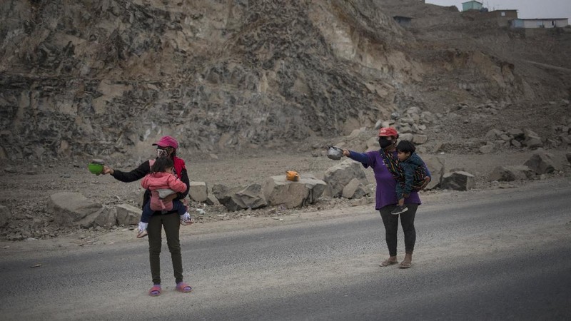 Jenny Diaz begs in the middle of a road while carrying her daughter Aina Flores, 1, on the outskirts of Lima, Peru, Saturday, Aug.22, 2020, amid the coronavirus pandemic. (AP Photo/Rodrigo Abd)