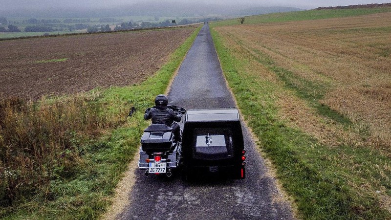 Joerg Grossmann drives his motorcycle combination with a Harley E Glide fitted with a sidecar on a road near Anspach, Germany, on Monday, Aug. 31, 2020. The 56 year old Grossmann who calls himself a chauffeur for the deceased, developed his motorbike hearse for die-hard bikers who want a last ride to their final resting place. in Frankfurt, (AP Photo/Michael Probst)