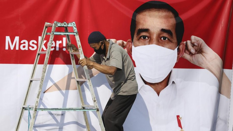 A worker climbs a ladder as he installs a coronavirus awareness-themed banner bearing a portrait of President Joko Widodo wearing a face mask, in Jakarta, Indonesia, Wednesday, Aug. 26, 2020. Writings on the banner read 