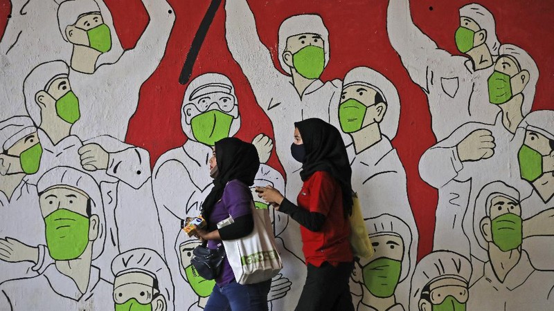 A worker climbs a ladder as he installs a coronavirus awareness-themed banner bearing a portrait of President Joko Widodo wearing a face mask, in Jakarta, Indonesia, Wednesday, Aug. 26, 2020. Writings on the banner read 
