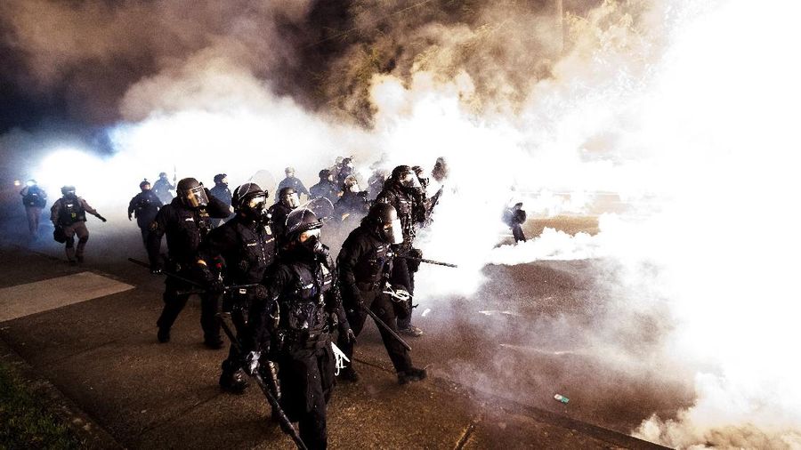 Police officers pass a fire lit by protesters on Saturday, Sept. 5, 2020, in Portland, Ore. Hundreds of people gathered for rallies and marches against police violence and racial injustice Saturday night in Portland, Oregon, as often violent nightly demonstrations that have happened for 100 days since George Floyd was killed showed no signs of ceasing. (AP Photo/Noah Berger)