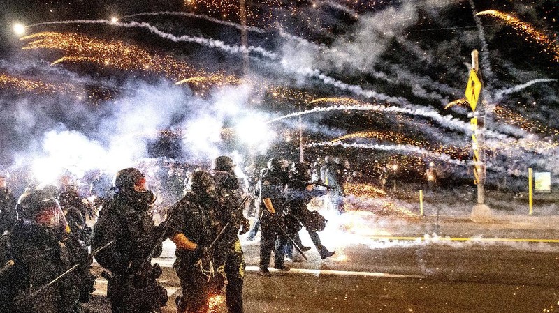 Police officers pass a fire lit by protesters on Saturday, Sept. 5, 2020, in Portland, Ore. Hundreds of people gathered for rallies and marches against police violence and racial injustice Saturday night in Portland, Oregon, as often violent nightly demonstrations that have happened for 100 days since George Floyd was killed showed no signs of ceasing. (AP Photo/Noah Berger)