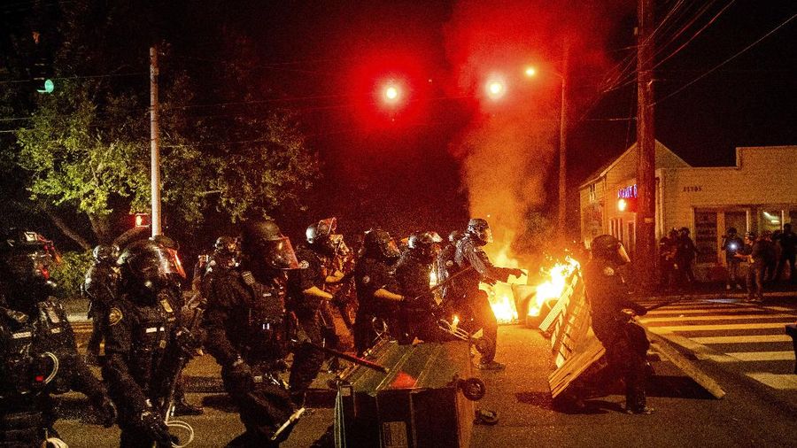 Police officers pass a fire lit by protesters on Saturday, Sept. 5, 2020, in Portland, Ore. Hundreds of people gathered for rallies and marches against police violence and racial injustice Saturday night in Portland, Oregon, as often violent nightly demonstrations that have happened for 100 days since George Floyd was killed showed no signs of ceasing. (AP Photo/Noah Berger)