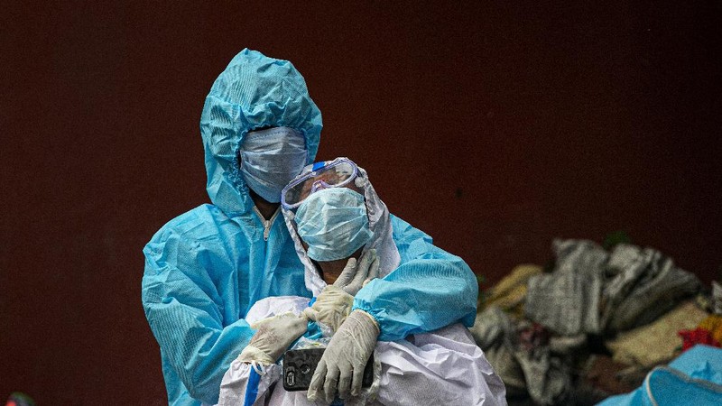 A woman wearing white protective gear, foreground, mourns after taking a glimpse of her husband's body, a victim of COVID 19, at a cremation site in Gauhati, India, Thursday, Sept. 10, 2020. Experts caution that India's outbreak is entering a more dangerous phase as the virus spreads to smaller towns and villages. (AP Photo/Anupam Nath)