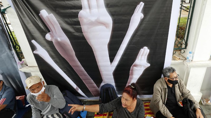 Pro-democracy protesters sit in front of a poster of the three finger symbol of resistance  during a protest outside Thammasat University in Bangkok, Thailand, Saturday, Sept. 19, 2020. Protesters gathered Saturday in Bangkok for what was expected to be the biggest rally yet in an ongoing campaign calling for a new election and democratic reforms. (AP Photo/Sakchai Lalit)