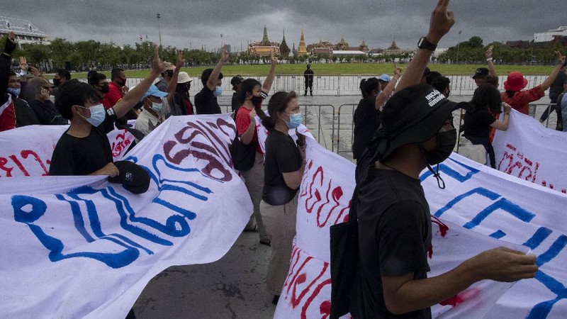 Pro-democracy protesters sit in front of a poster of the three finger symbol of resistance  during a protest outside Thammasat University in Bangkok, Thailand, Saturday, Sept. 19, 2020. Protesters gathered Saturday in Bangkok for what was expected to be the biggest rally yet in an ongoing campaign calling for a new election and democratic reforms. (AP Photo/Sakchai Lalit)