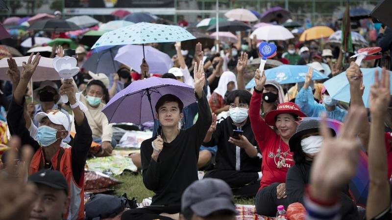 Pro-democracy protesters sit in front of a poster of the three finger symbol of resistance  during a protest outside Thammasat University in Bangkok, Thailand, Saturday, Sept. 19, 2020. Protesters gathered Saturday in Bangkok for what was expected to be the biggest rally yet in an ongoing campaign calling for a new election and democratic reforms. (AP Photo/Sakchai Lalit)
