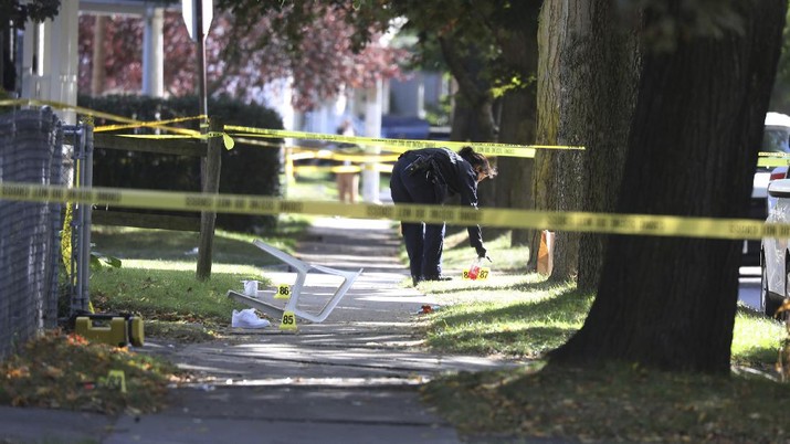 A Rochester police technician picks up some items as evidence near the home where a fatal house party took place, Saturday, Sept. 19, 2020, in Rochester, N.Y. A pair of sneaker are scattered around a tipped chair. Police in Rochester, New York, say several people died and others were wounded by gunfire at a backyard party early Saturday. (Tina MacIntyre-Yee/Democrat & Chronicle via AP)