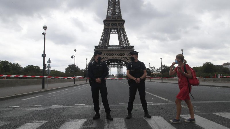 A Russian tourist holding a bottle of Champagne walks past police officers securing the bridge leading to the Eiffel Tower, Wednesday, Sept. 23, 2020 in Paris. Paris police have blockaded the area around the Eiffel Tower after a phone-in bomb threat. (AP Photo/Michel Euler)