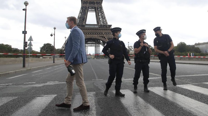 A Russian tourist holding a bottle of Champagne walks past police officers securing the bridge leading to the Eiffel Tower, Wednesday, Sept. 23, 2020 in Paris. Paris police have blockaded the area around the Eiffel Tower after a phone-in bomb threat. (AP Photo/Michel Euler)