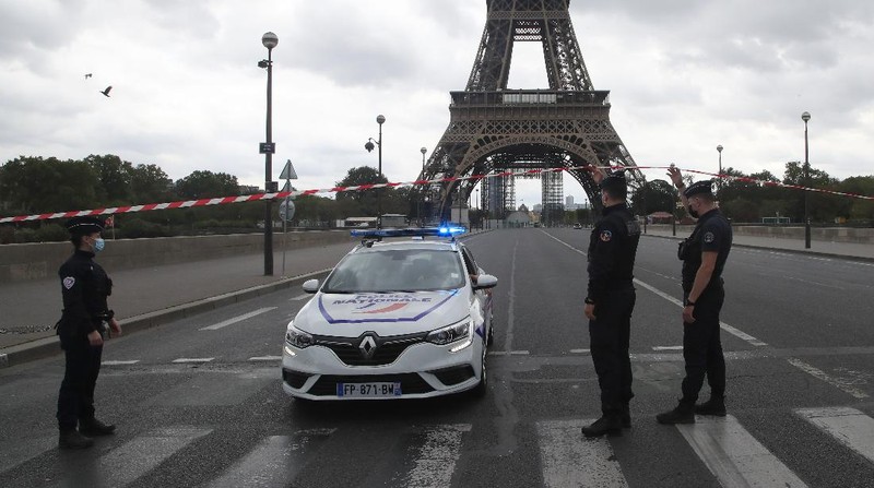 A Russian tourist holding a bottle of Champagne walks past police officers securing the bridge leading to the Eiffel Tower, Wednesday, Sept. 23, 2020 in Paris. Paris police have blockaded the area around the Eiffel Tower after a phone-in bomb threat. (AP Photo/Michel Euler)